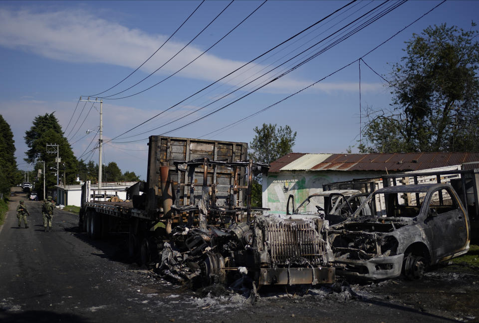 Mexican Army soldiers walk around the burnt-out remains of several trucks that were torched during a protest against a raid targeting illegal logging and sawmills in the pine forests outside of Huitzilac, Mexico, Wednesday, Aug. 2, 2023. Morelos state prosecutors said the raid involved at least 300 officers of the state police, the National Guard and the army. (AP Photo/Eduardo Verdugo)