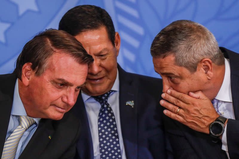 El presidente de Brasil, Jair Bolsonaro, escucha a su jefe de Estado Mayor cerca del vicepresidente de Brasil durante una ceremonia en Brasilia