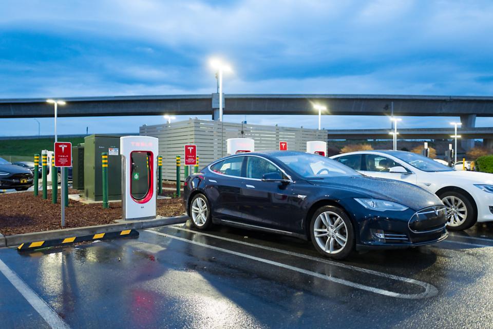 At dusk, Tesla Motors electric cars are plugged in and charging at a Tesla Supercharger electric vehicle charger in Pleasanton, California, March 12, 2018.