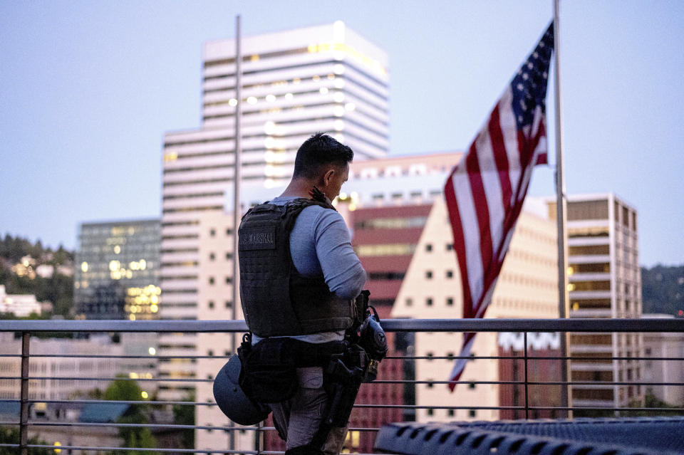 FILE - In this July 26, 2020, file photo, after a night of facing off against protesters, a deputy U.S. marshal takes a break on a rooftop terrace at the Mark O. Hatfield U.S. Courthouse in Portland, Ore. Once hailed as one of the most livable cities in the U.S., Portland, Oregon, is grappling with an uncertain future as it reaches a stunning benchmark: 100 consecutive nights of racial injustice protests marred by vandalism, chaos — and now, the killing of a supporter of President Donald Trump. (AP Photo/Noah Berger, File)