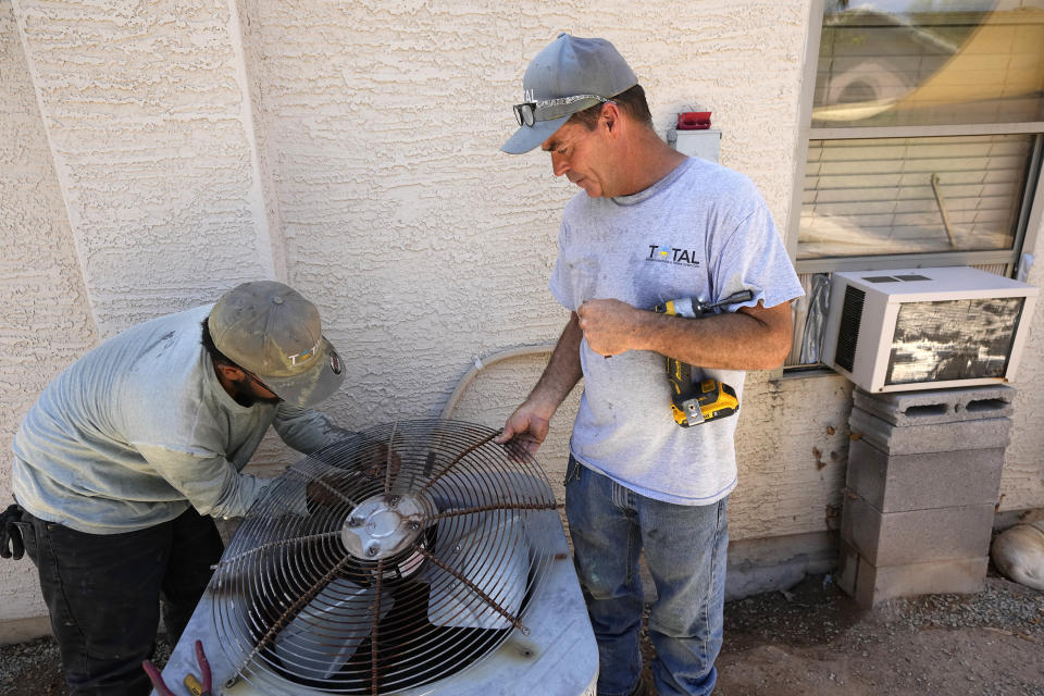 FILE - JP Lantin, right, owner of Total Refrigeration, and service tech Michael Villa, work on replacing a fan motor on an air conditioning unit July 19, 2023, in Laveen, Ariz. (AP Photo/Ross D. Franklin, File)