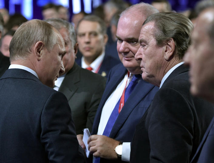 Russian President Vladimir Putin and former German Chancellor Gerhard Schroeder stand facing each other among a group of others.
