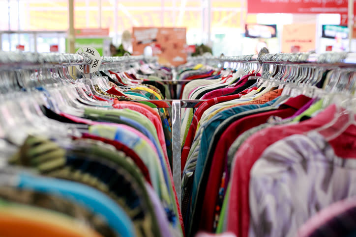 Racks of assorted clothes in a thrift store, displayed tightly together on hangers. Various styles and sizes are visible