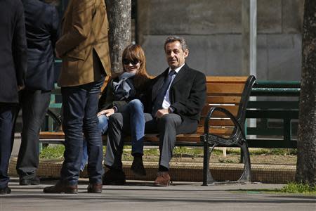 Former French President Nicolas Sarkozy (R) sits on a bench with his wife and singer Carla Bruni-Sarkozy after voting at a polling station in the first round in the French mayoral elections in Paris, March 23, 2014. REUTERS/Benoit Tessier