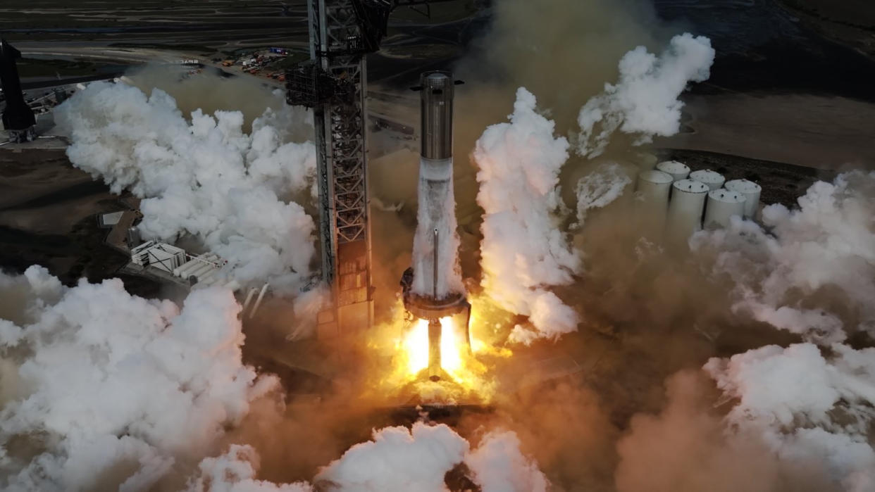  A giant silver rocket booster tests its engines on the launch pad. 