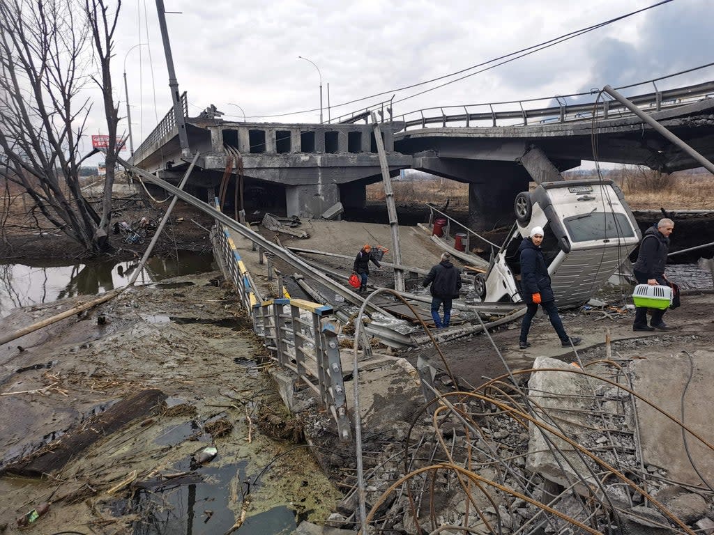 Pedestrians cross a destroyed bridge as they evacuate the city of Irpin, northwest of Kyiv, 6 March 2022 (AFP via Getty Images)