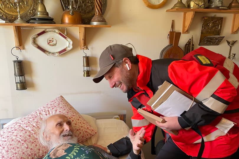 A postman talking to an ill man in bed