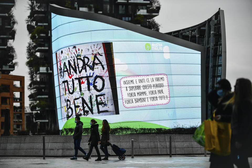 People walk past a billboard reading "Everything will be alright", in Milan, Italy. The nationwide lockdown to slow coronavirus is still early days for much of Italy, but Italians are already are showing signs of solidarity. This week, children’s drawings of rainbows are appearing all over social media as well as on balconies and windows in major cities ready, ‘’Andra’ tutto bene,’’ Italian for ‘’Everything will be alright.’’ For most people, the new coronavirus causes only mild or moderate symptoms. For some, it can cause more severe illness, especially in older adults and people with existing health problems. (Claudio Furlan/LaPresse via AP)