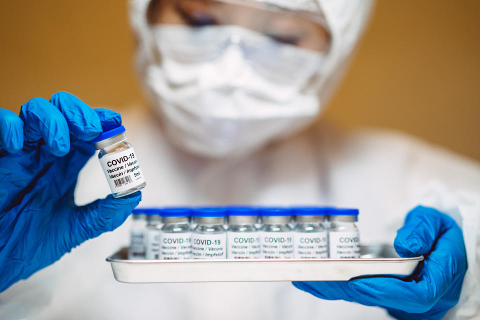 Healthcare professional in protective gloves & workwear holding & organising a tray of COVID-19 vaccine vials. The professional is carrying out researches on COVID-19 vaccine in laboratory.