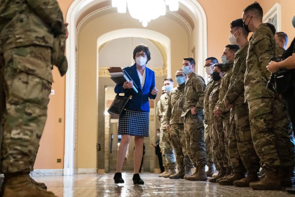 A senator stands in front of a group of troops in camo fatigues