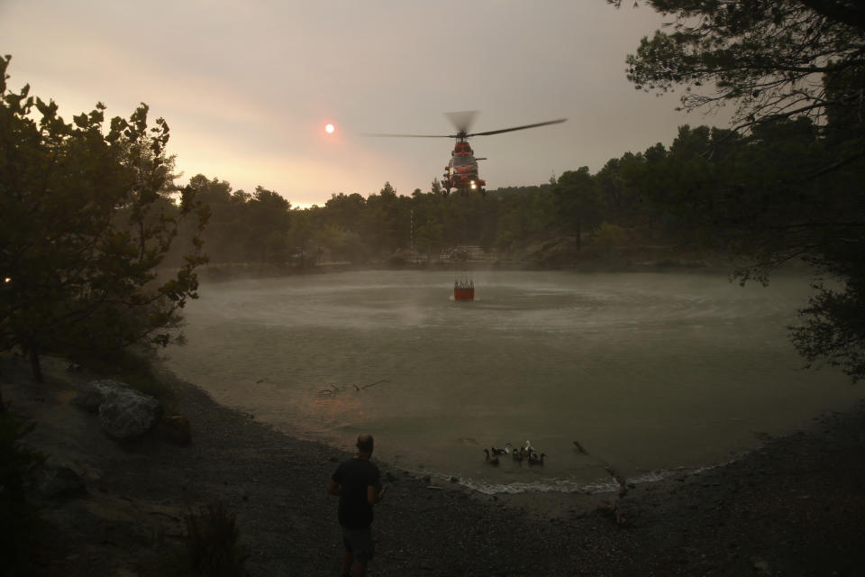 A firefighting helicopter loads water from a lake, as it participates in an operation against, a wildfire in northern Athens, Saturday, Aug. 7, 2021. Wildfires rampaged through Greek forests for yet another day Saturday, threatening homes and triggering more evacuations a day after hundreds of people were plucked off beaches by ferries in a dramatic overnight rescue. (AP Photo/Lefteris Pitarakis)