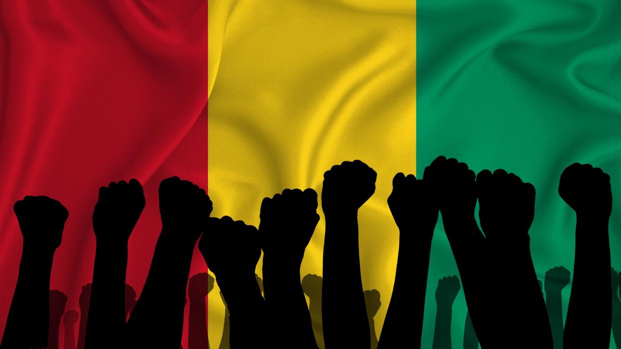  Silhouette of raised arms and clenched fists on the background of the flag of Guinea. The concept of power, conflict.  