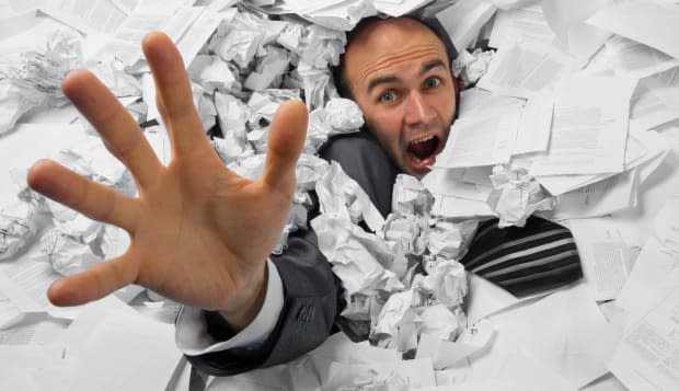 Businessman sinking in heap of documents and asking for help