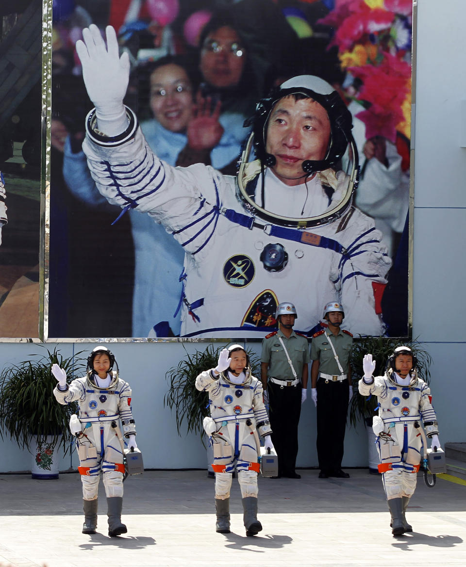 FILE - In this June 16, 2012 file photo, Chinese astronauts from left, Liu Yang, Jing Haipeng and Liu Wang wave and walk before a giant portrait of China's first astronaut Yang Liwei, as they depart for the Shenzhou 9 spacecraft rocket launch pad at the Jiuquan Satellite Launch Center in Jiuquan, China. China's landing of its third probe on the moon is part of an increasingly ambitious space program that has a robot rover en route to Mars, is developing a reusable space plane and plans to put humans back on the lunar surface. (AP Photo/Ng Han Guan, File)