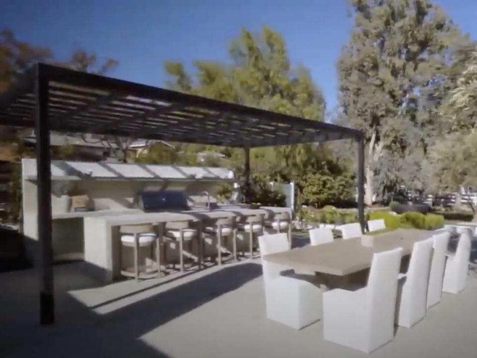 An outdoor kitchen covered by a pagoda and a large table.