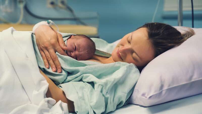 A mom holds a newborn baby while lying in a hospital bed