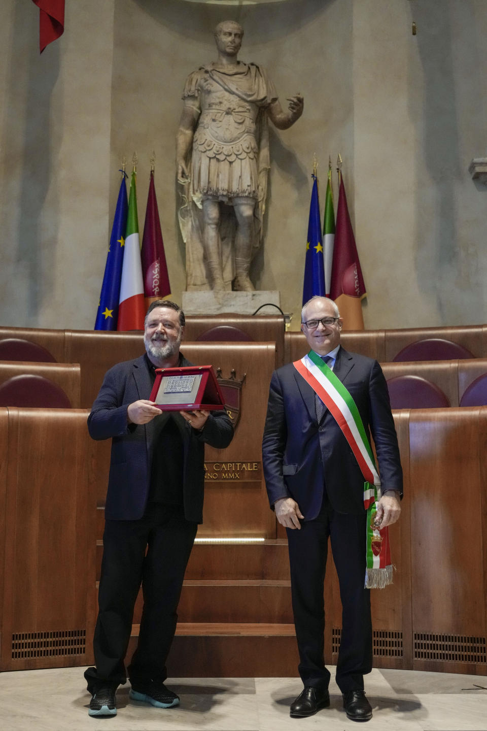 Actor Russel Crowe, left, poses under a statue of ancient Roman emperor Julius Cesar with the "Ambassador of Rome in the World" award he received from Rome's mayor Roberto Gualtieri, in Rome's Capitol Hill, Friday, Oct. 14, 2022. (AP Photo/Andrew Medichini)