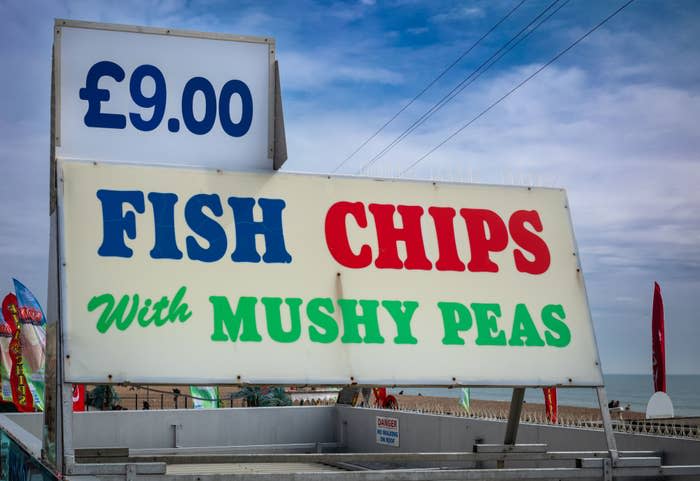 Sign advertising "Fish & Chips with Mushy Peas" for £9.00, set against a sky backdrop