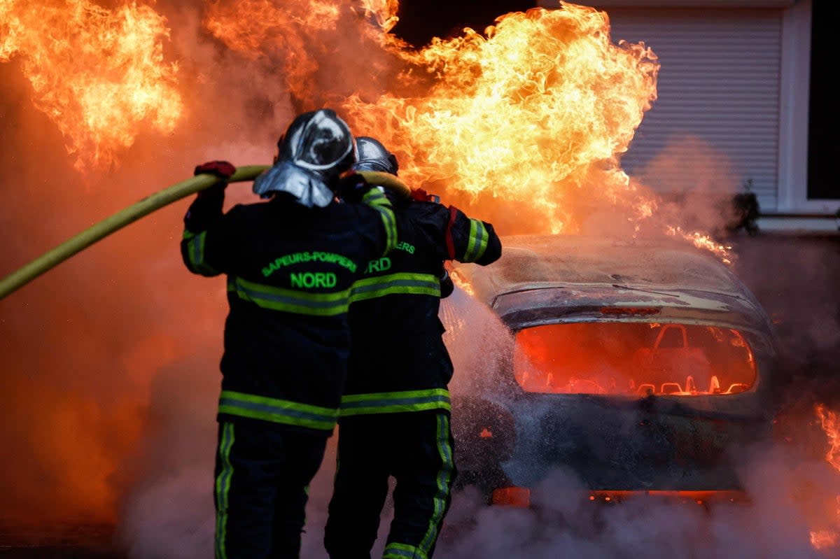 Firefighters put out a burning car during protests in Lille, on Thursday  (AFP via Getty Images)