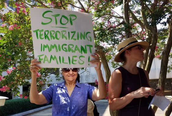 a demonsytrator holds a sign reading "stop terrorizing immigrant families"