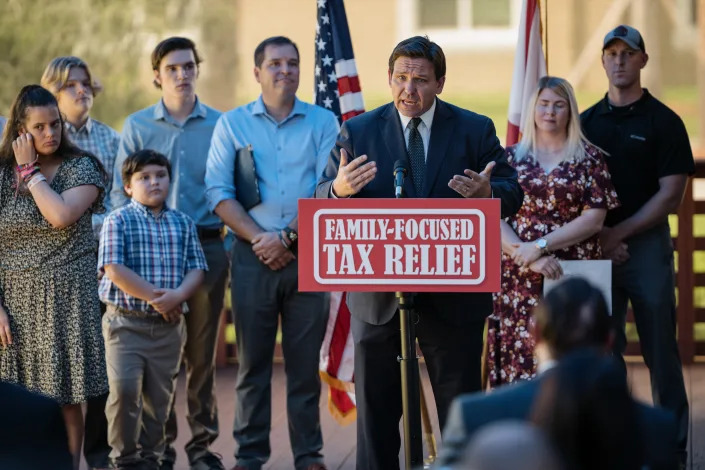 Gov. Ron DeSantis addresses a press conference at a podium marked: Family-Focused Tax Relief, surrounded by mostly young supporters. 