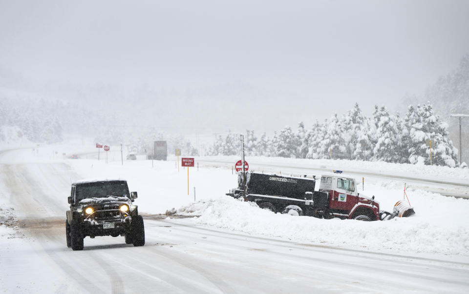 A jeep passes a stranded snowplow while traveling west of Ute Pass on U.S. Highway 24 toward Woodland Park, Colo., Thursday, March 14, 2024. A major storm is dumping heavy, wet snow in Colorado — forcing flight cancellations and shutting down a highway that connects Denver to Colorado ski resorts. (Christian Murdock/The Gazette via AP)