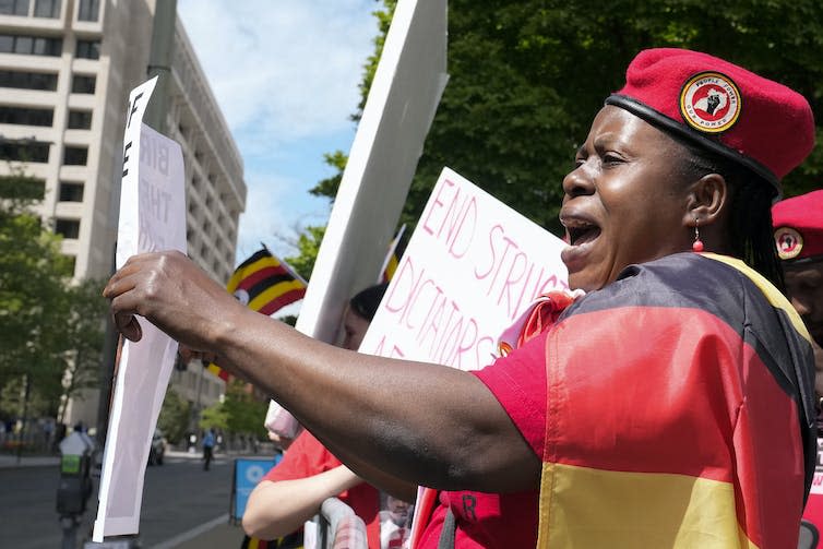a woman draped in a black, yellow and red — the colours of the Ugandan flag — shouts at a protest