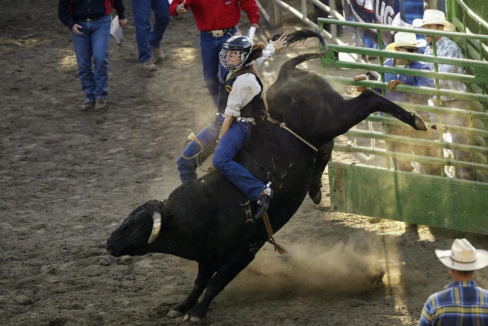 Woman in helmet on bucking bull in a rodeo ring