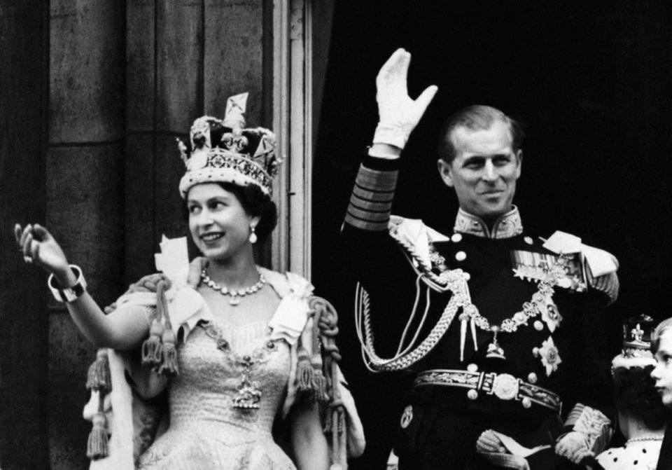 The Queen wearing the Imperial State Crown and Prince Philip, the Duke of Edinburgh in uniform of Admiral of the Fleet wave from the balcony to the onlooking crowds around the gates of Buckingham Palace after the Coronation in 1953 (PA)