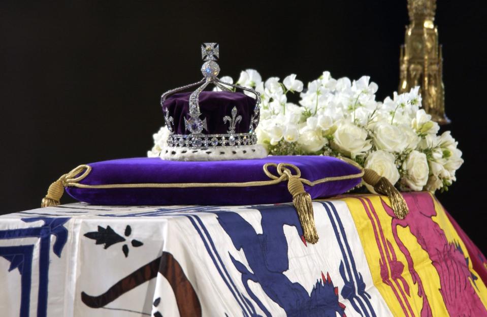 a purple crown sits atop a purple cushion on a coffin draped with flowers and cloth