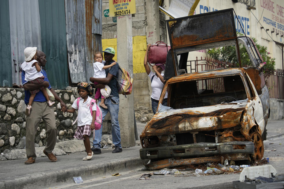 FILE - Residents walk past a burnt car as they evacuate the Delmas 22 neighborhood due to gang violence in Port-au-Prince, Haiti, May 2, 2024. Thousands of people in Haiti have been driven from their homes by gang violence. (AP Photo/Ramon Espinosa, File)