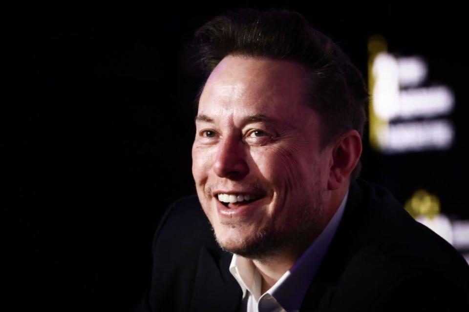 Elon Musk smiling in black suit with white shirt