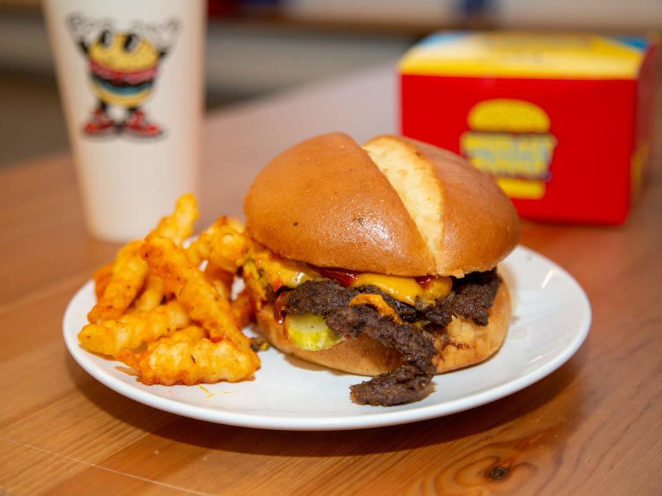 A burger and fries on a plate in front of a cup and box