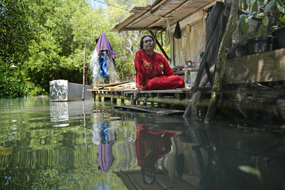 Munadiroh sits outside her home in Mondoliko, Central Java, Indonesia, Monday, Aug. 1, 2022. Her child makes the long journey to school by wading through the water and riding in a boat several times a week. (AP Photo/Dita Alangkara)