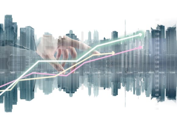 A hand plots a stock chart over a cityscape