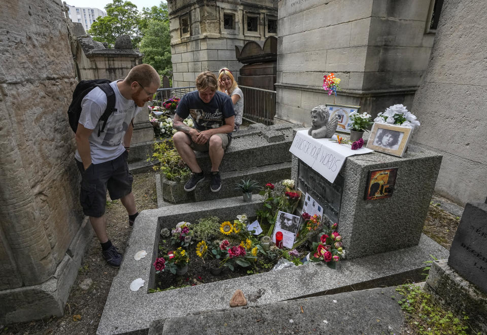 Joachim Tittmar from Germany, left, Walter Homburg of Netherland, center, and his girlfriend Kate Schirm gather at the tomb of rock singer Jim Morrison at the Pere-Lachaise cemetery in Paris, Saturday, July 3, 2021. Fans across Europe gathered at the grave of rock legend Jim Morrison to mark the 50th anniversary of his death. (AP Photo/Michel Euler)