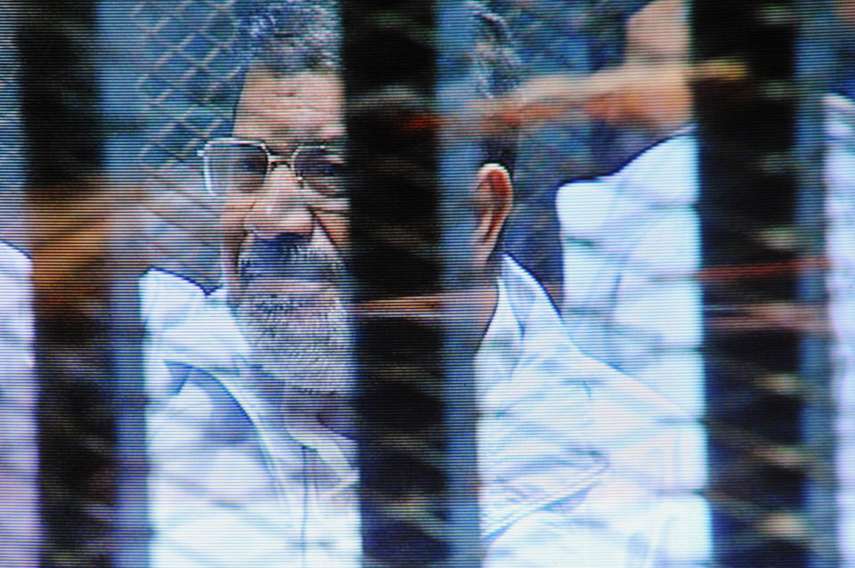 FILE - In this Sunday, Feb. 16, 2014 file photo, Egypt's ousted President Mohammed Morsi in a soundproof barred glass cage is seen on a monitor set up outside a courtroom where Morsi and 35 others are facing charges of conspiring with foreign groups and undermining national security, in Cairo, Egypt. Morsi, toppled in July by the military, faces a host of criminal charges and appeared in court Saturday, Feb. 22, 2014, in a case that charges him and 130 others over prison breaks that freed some 20,000 inmates during the 18-day revolt in 2011 that toppled autocrat Hosni Mubarak. Morsi himself was freed in a prison break before becoming the nation’s first freely elected president. (AP Photo/Mohammed al-Law, File)