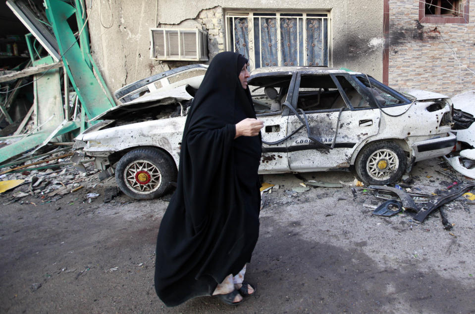 A woman walks past the site of a car bomb attack in Baghdad, Iraq, Tuesday, Feb. 18, 2014. A wave of explosions rocked mainly Shiite neighborhoods in Baghdad shortly after sunset on Monday, killing and wounding scores of people, said Iraqi officials. (AP Photo/Hadi Mizban)