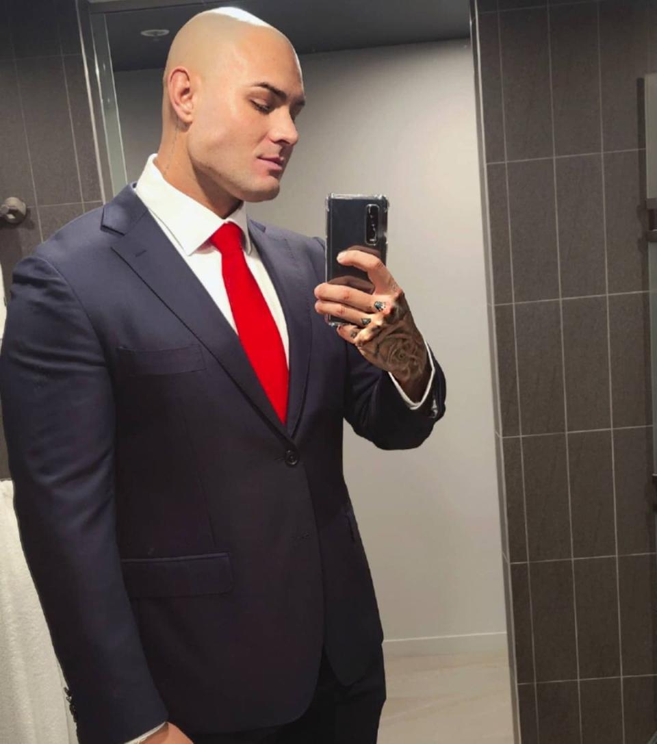 MAFS' Sam Ball wearing a blue suit and a red tie. His head is shaved