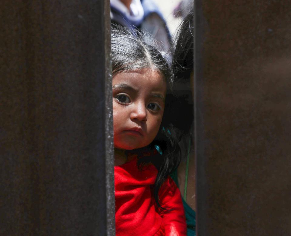A small girl peers through the border fence near Monument Rd. close to the International Wastewater Treatment Plant in San Diego, Calif., May 11, 2023. 