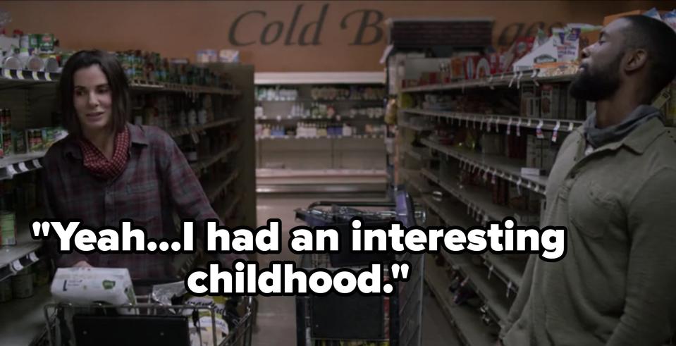 Sandra Bullock and Trevante Rhodes are shopping in a grocery store aisle, pushing carts filled with various items and standing in front of a "Cold Beverages" sign