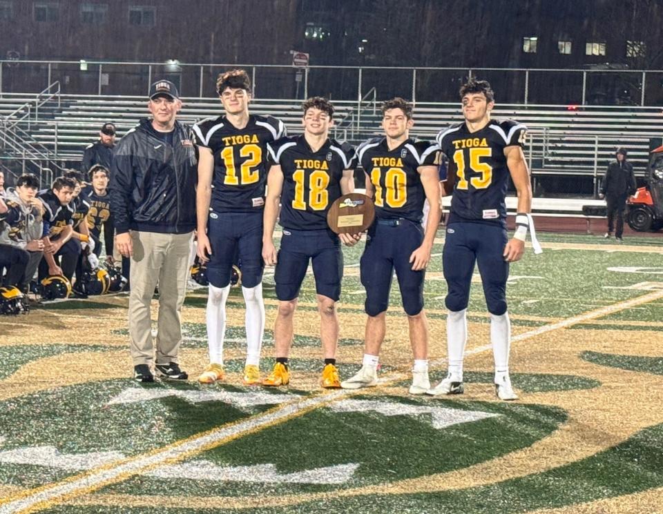 Tioga head coach Nick Aiello, left, with Tigers players Gavin Fisher (12), Caden Bellis (18), Drew Macumber (10) and Valentino Rossi (15) as they hold the plaque after a 56-12 victory over Dolgeville in a NYSPHSAA Class D regional final Nov. 17, 2023 at Vestal.