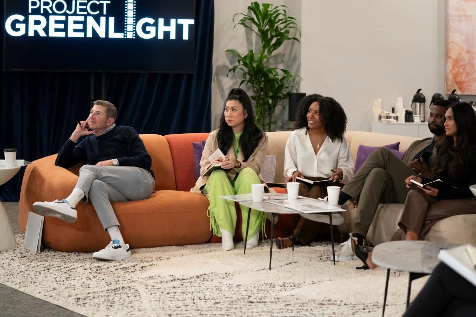 A group of producers sit on a couch with notebooks, watching something O.S. The words "Project Greenlight" are visible in white on a black background behind them.