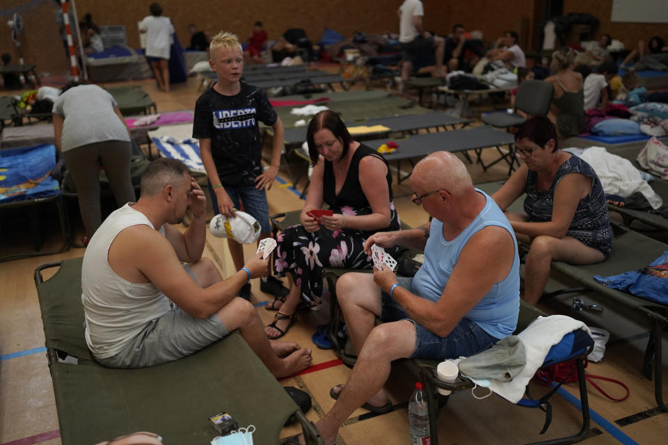 Evacuated campers play cards in a gymnasium in Bormes-les-Mimosas, southern France, Wednesday, Aug. 18, 2021. (AP Photo/Daniel Cole)