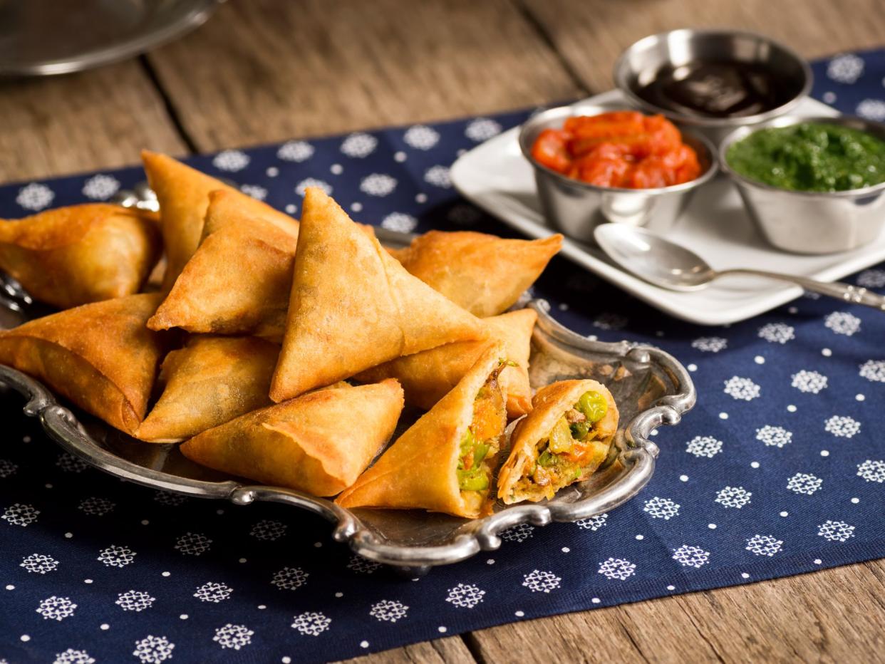 A plate of samosas - a vegetarian dish commonly found in Indian restaurants - with onion-tomato chutney, mint-coriander chutney and tamarind sauce for dipping.