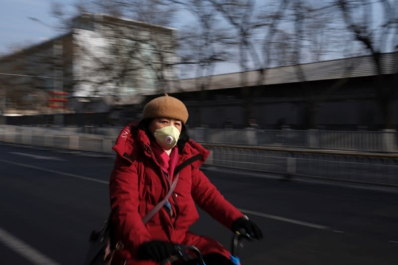 A woman wearing a protective mask rides her bicycle on a street in Beijing
