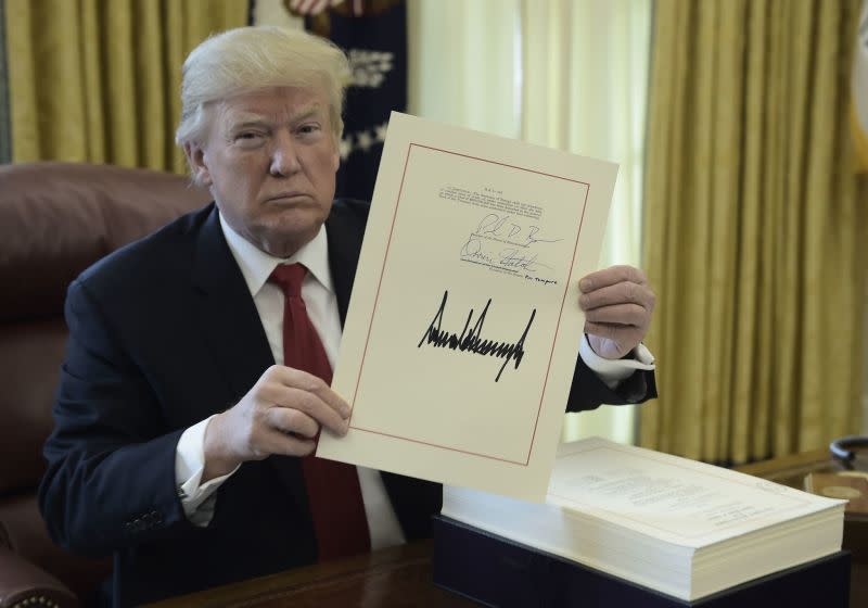 President Trump holds up a document during an event to sign the Tax Cut and Reform Bill in the Oval Office at The White House in Washington, DC on December 22, 2017.