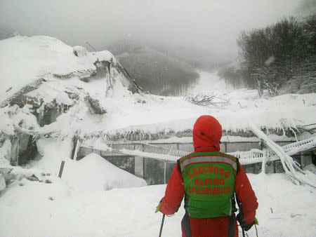 A member of Lazio's Alpine and Speleological Rescue Team stands in front of the Hotel Rigopiano in Farindola, central Italy, hit by an avalanche, in this January 19, 2017 handout picture provided by Lazio's Alpine and Speleological Rescue Team. Soccorso Alpino Speleologico Lazio/Handout via REUTERS