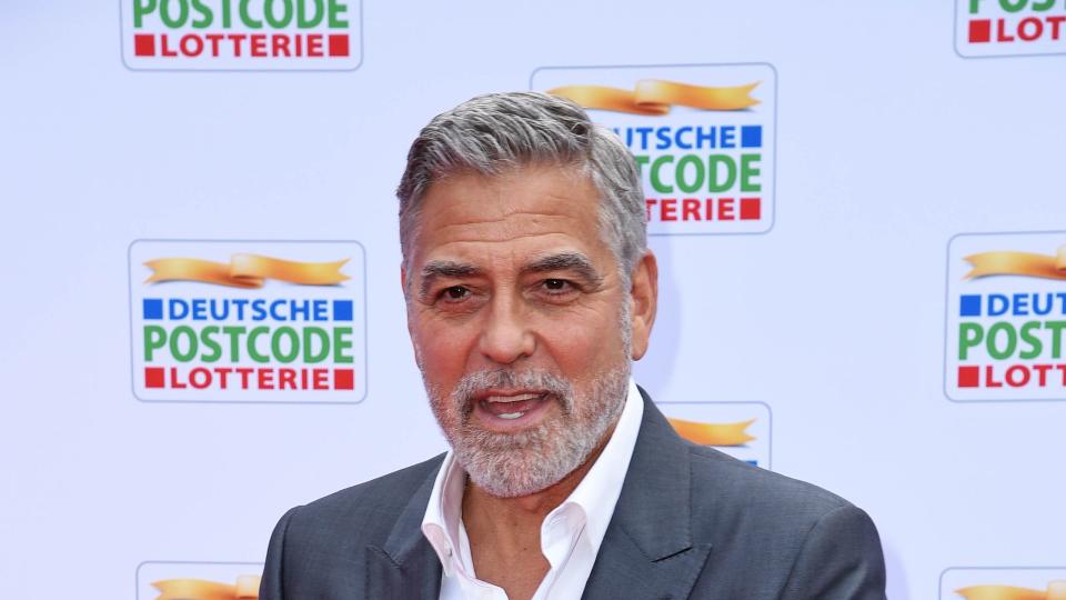 george clooney talking to photographers off camera as he poses on the red carpet