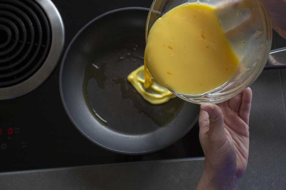 Pouring beaten egg mixture into frying pan.